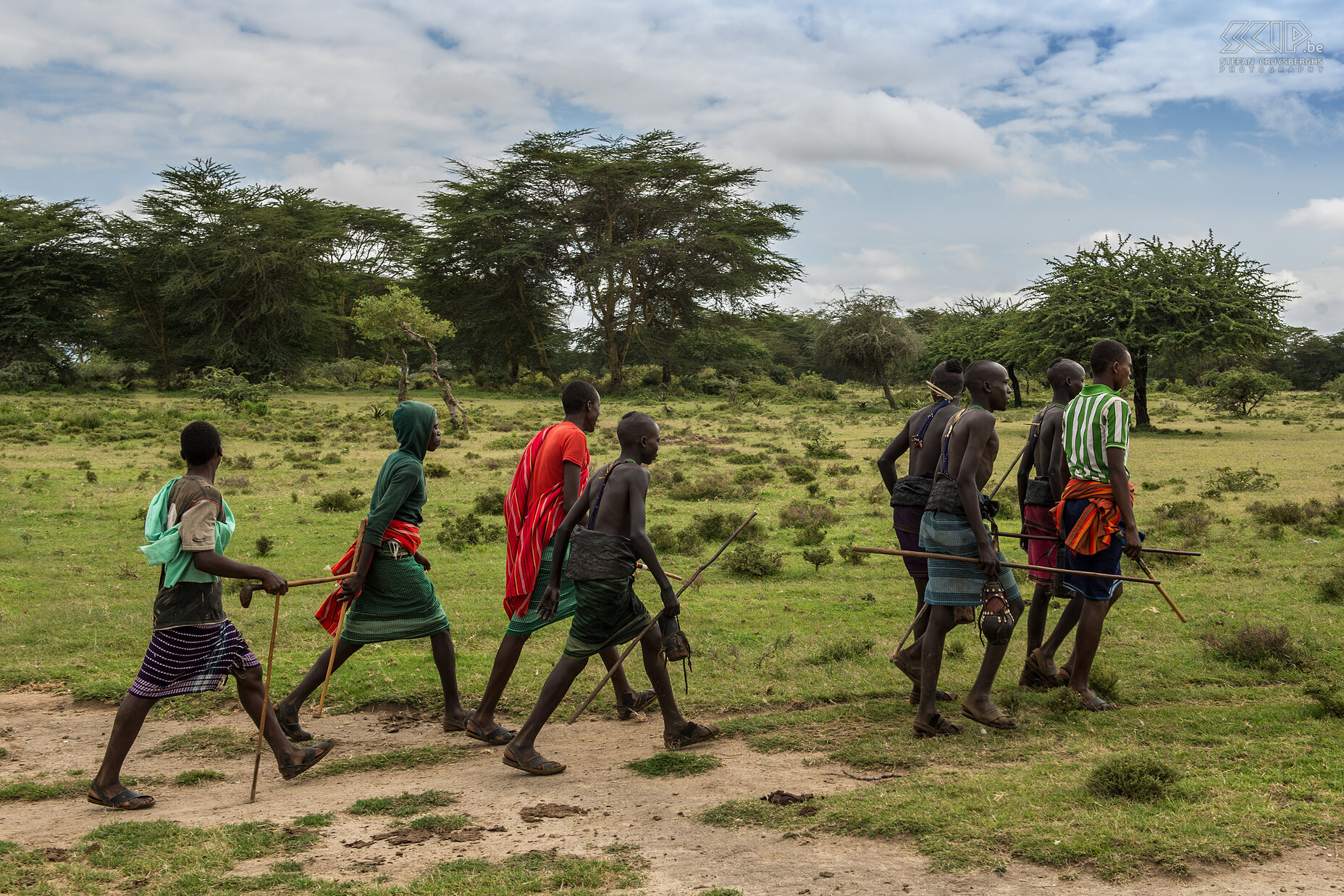 Kisima - Toekomstige morans Om de 6 à 10 jaar organiseren de Samburu clans een lmuget-ceremonie voor de overgang naar een volgende leeftijdsgroep. Jonge mannen van 14 tot 20 jaar worden besneden en worden daarna moran (krijger). Dit is de belangrijkste gebeurtenis in het leven van een jonge Samburu. <br />
<br />
De dagen voor de lmuget ceremonies verlaten ze de lorora (het tijdelijke dorp) en in groep gaan ze al zingend op pad om water en kruiden te verzamelen. Sommigen van hen dragen nog steeds de traditionele door-houtskool-zwartgeblakerde-mantel rond hun middel. Ze zingen de lebarta, een speciaal lied voor de besnijdenis. Stefan Cruysberghs